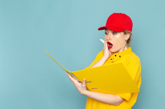 Vue de face jeune courrier en chemise jaune et cape rouge tenant un fichier jaune en écrivant des notes sur les émotions des travailleurs de l'espace bleu