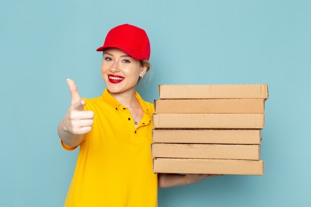 Vue de face jeune courrier en chemise jaune et cape rouge tenant des paquets avec le sourire sur le travailleur de l'espace bleu