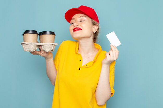 Vue de face jeune courrier en chemise jaune et cape rouge tenant des tasses à café en plastique carte blanche sur l'espace bleu