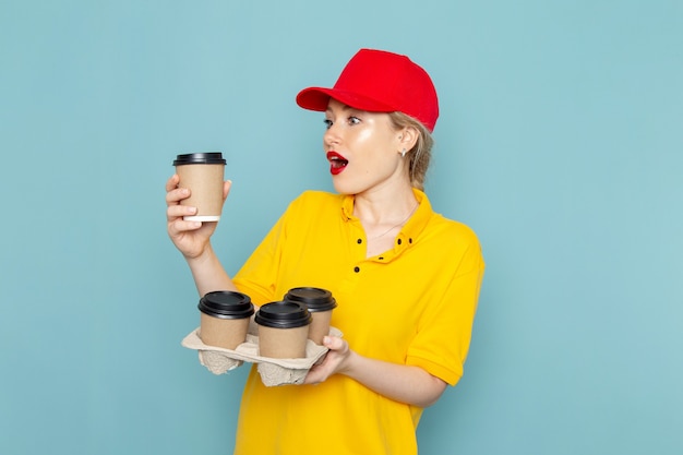 Vue de face jeune courrier en chemise jaune et cape rouge tenant des tasses à café sur le travail de l'espace bleu