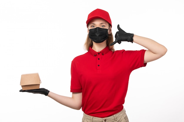 Une vue de face jeune courrier en chemise rouge bonnet rouge gants noirs et masque noir tenant le paquet alimentaire