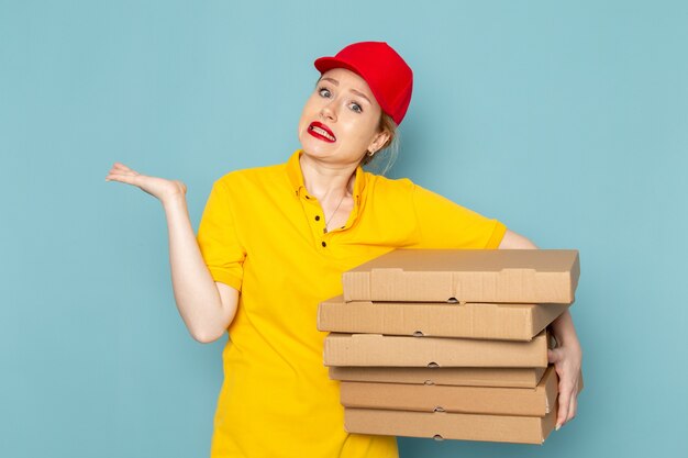 Vue de face jeune courrier féminin en chemise jaune et cape rouge tenant des paquets sur le travailleur de l'espace bleu