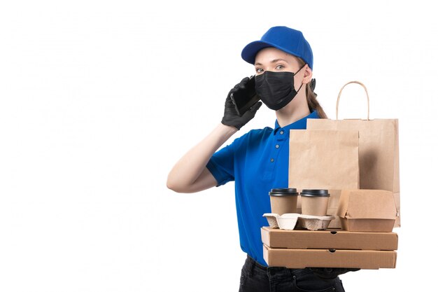 Une Vue De Face Jeune Courrier En Uniforme Bleu Gants Noirs Et Masque Noir Tenant Des Colis De Livraison De Nourriture Et Smartphone