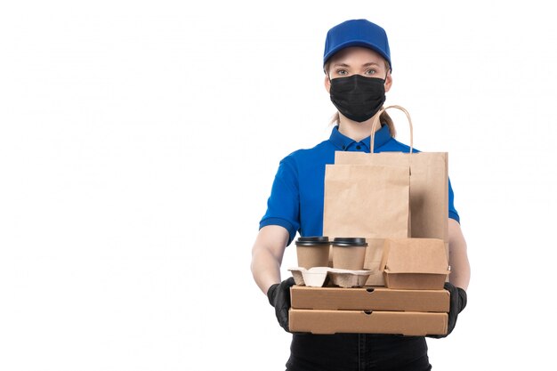 Une vue de face jeune courrier en uniforme bleu gants noirs et masque noir tenant des colis de livraison de nourriture