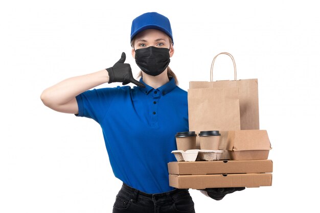 Une vue de face jeune courrier en uniforme bleu gants noirs et masque noir tenant des colis de livraison de nourriture