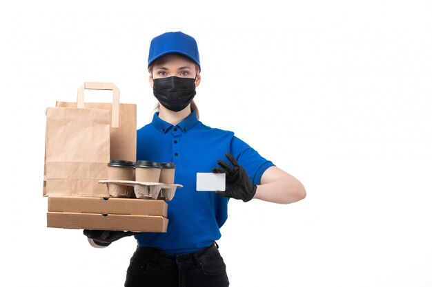 Une vue de face jeune courrier en uniforme bleu gants noirs et masque noir tenant des colis de livraison de nourriture