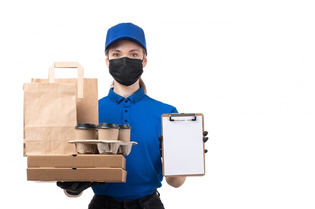 Une vue de face jeune courrier en uniforme bleu gants noirs et masque noir tenant des colis de livraison de nourriture