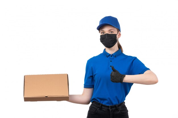 Une vue de face jeune courrier en uniforme bleu gants noirs et masque noir tenant le paquet de livraison de nourriture