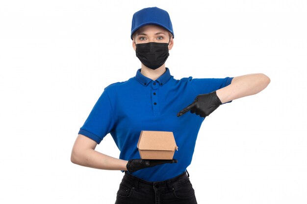 Une vue de face jeune courrier en uniforme bleu masque noir et gants tenant le paquet de livraison de nourriture