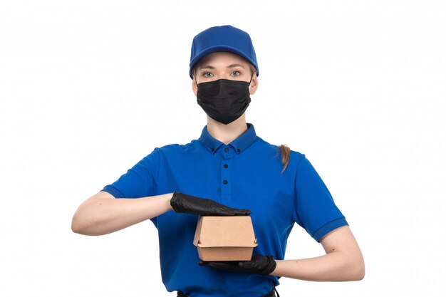 Une vue de face jeune courrier en uniforme bleu masque noir et gants tenant le paquet de livraison de nourriture