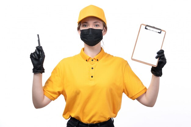 Une vue de face jeune courrier en uniforme jaune gants noirs et masque noir tenant le bloc-notes