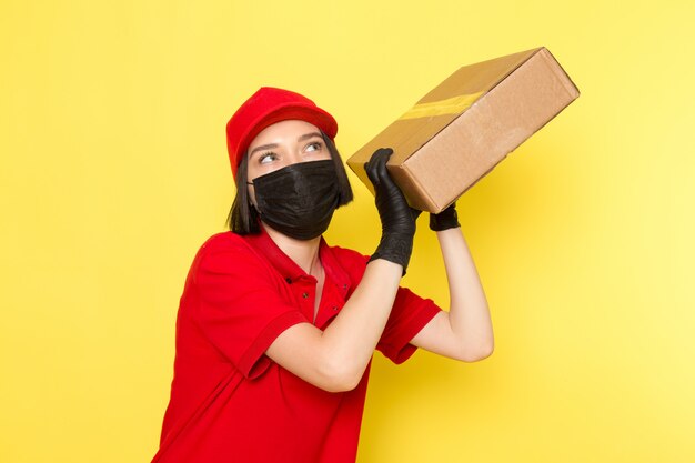 Une vue de face jeune courrier en uniforme rouge gants noirs et bonnet rouge tenant la boîte de nourriture