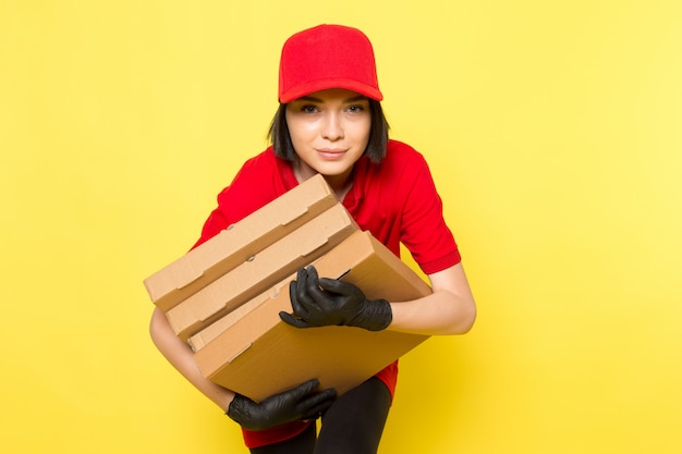 Une vue de face jeune courrier en uniforme rouge gants noirs et bonnet rouge tenant des boîtes de nourriture