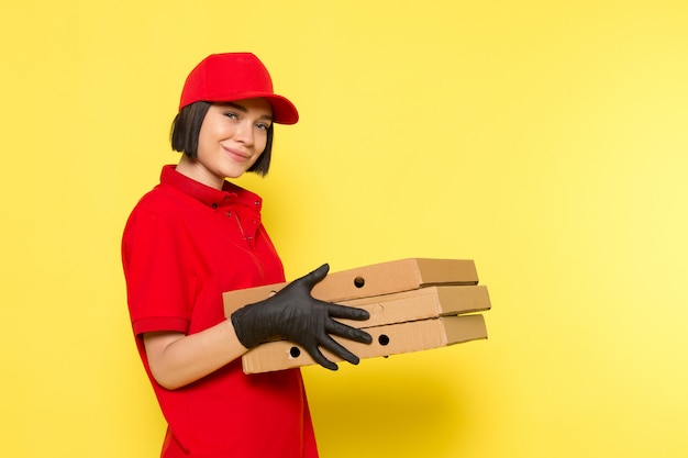 Une vue de face jeune courrier en uniforme rouge gants noirs et bonnet rouge tenant des boîtes de nourriture