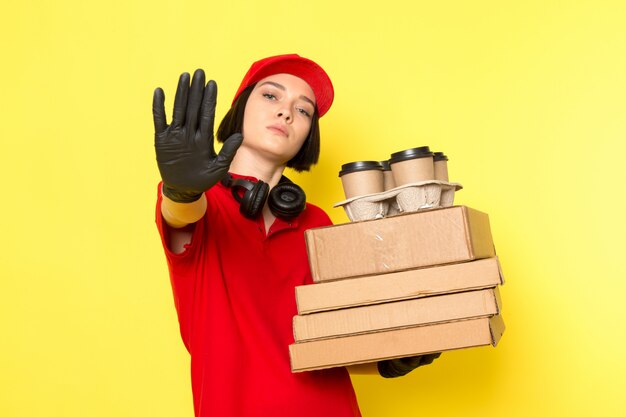 Photo gratuite une vue de face jeune courrier en uniforme rouge gants noirs et bonnet rouge tenant des boîtes de nourriture