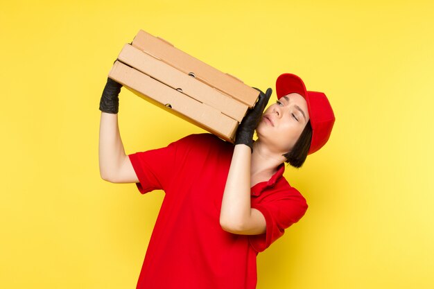 Une vue de face jeune courrier en uniforme rouge gants noirs et bonnet rouge tenant des boîtes