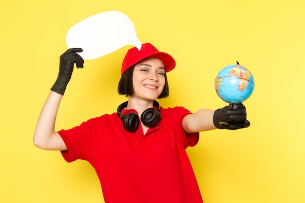 Une vue de face jeune courrier en uniforme rouge gants noirs et bonnet rouge tenant une pancarte blanche et petit globe