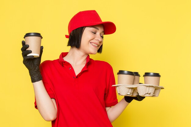 Une vue de face jeune courrier en uniforme rouge gants noirs et bonnet rouge tenant des tasses à café