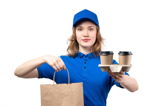 Une vue de face jeune courrier en uniforme tenant des colis de livraison et des tasses de café souriant