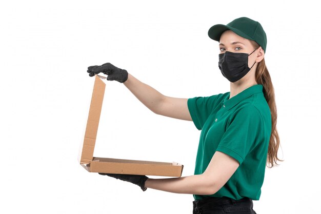Une vue de face jeune courrier en uniforme vert gants noirs et masque noir tenant le colis de livraison de nourriture