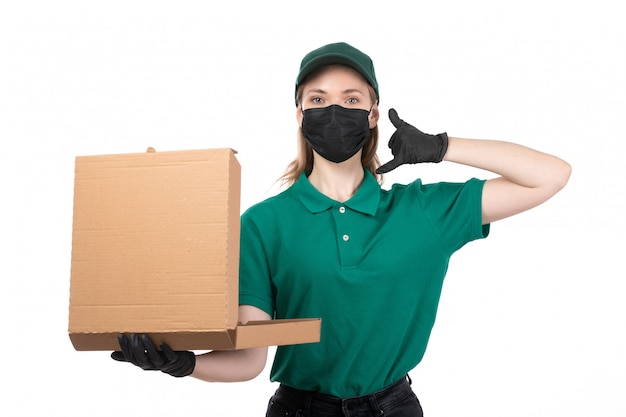 Une vue de face jeune courrier en uniforme vert gants noirs et masque noir tenant le colis de livraison de nourriture