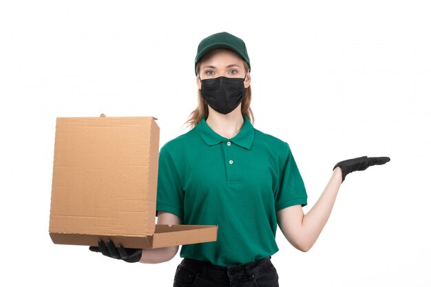 Une vue de face jeune courrier en uniforme vert gants noirs et masque noir tenant le colis de livraison de nourriture