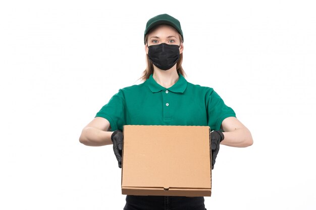 Une vue de face jeune courrier en uniforme vert gants noirs et masque noir tenant le colis de livraison de nourriture