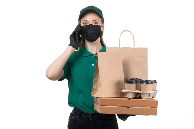 Une vue de face jeune courrier en uniforme vert gants noirs et masque noir tenant des colis de livraison de nourriture