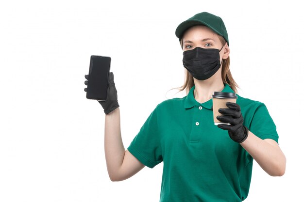 Une vue de face jeune courrier en uniforme vert gants noirs et masque noir tenant le paquet de livraison de nourriture et téléphone