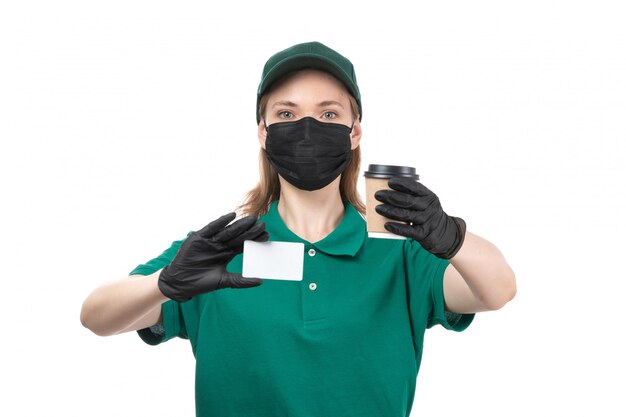 Une vue de face jeune courrier en uniforme vert gants noirs et masque noir tenant une tasse de café
