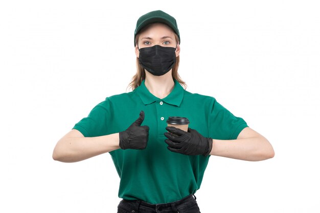 Une vue de face jeune courrier en uniforme vert gants noirs et masque noir tenant une tasse de café