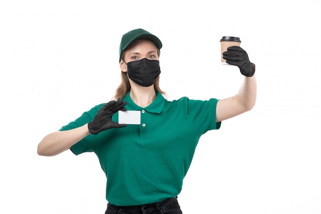 Une vue de face jeune courrier en uniforme vert gants noirs et masque noir tenant une tasse de café