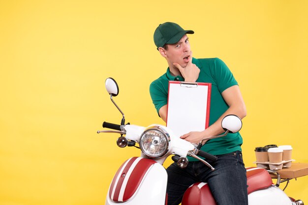 Vue de face jeune coursier masculin en uniforme vert avec du café sur jaune