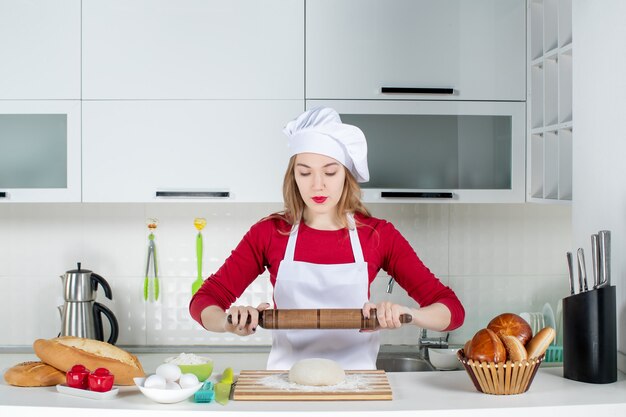 Vue de face jeune cuisinière commençant à rouler la pâte dans la cuisine