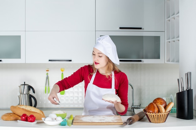 Vue de face jeune cuisinière saupoudrant de farine sur une planche à découper dans la cuisine