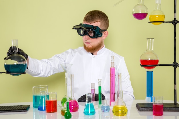 Vue de face jeune étudiant inspecte un nouveau produit chimique dans des lunettes de protection