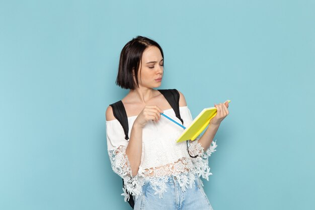 Vue de face de la jeune étudiante en chemise blanche jeans bleu et sac noir écrit des notes