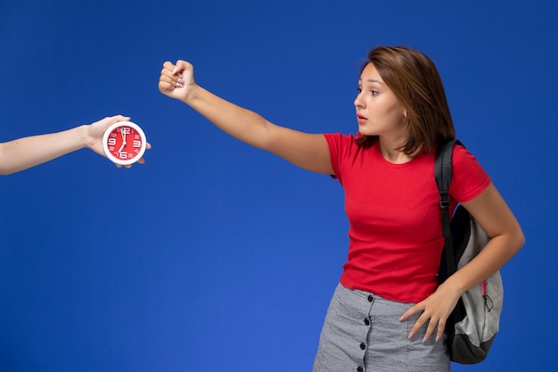 Vue de face jeune étudiante en chemise rouge portant un sac à dos menace sur fond bleu clair.