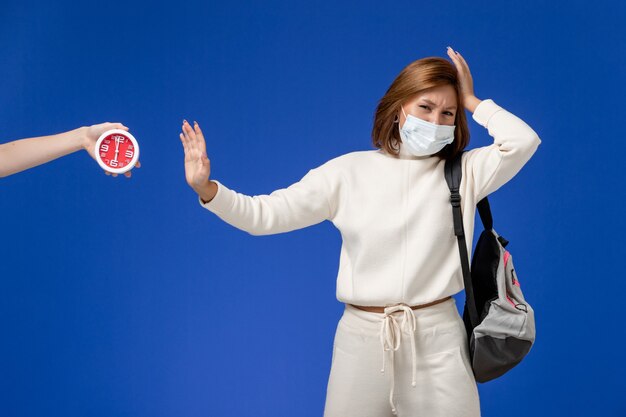 Vue de face jeune étudiante en maillot blanc portant un masque et un sac sur le mur bleu