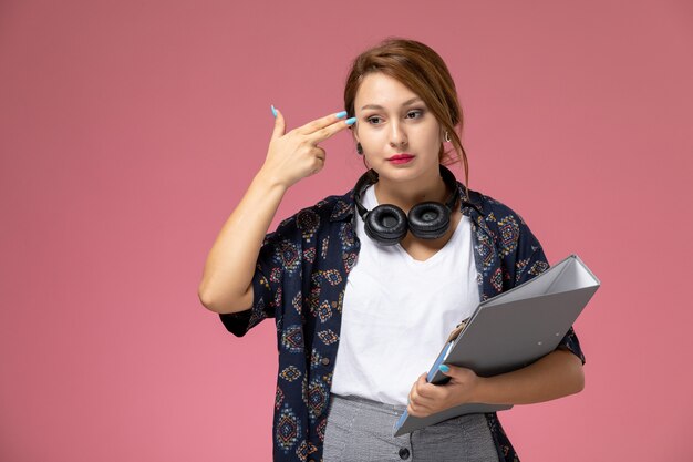 Vue de face jeune étudiante en t-shirt blanc et pantalon gris posant et pensant sur fond rose leçons étudiantes college college