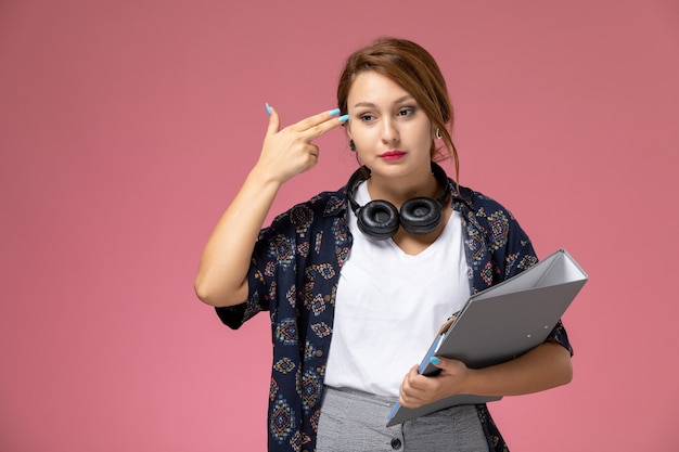 Vue de face jeune étudiante en t-shirt blanc et pantalon gris posant et pensant sur fond rose leçons étudiantes college college