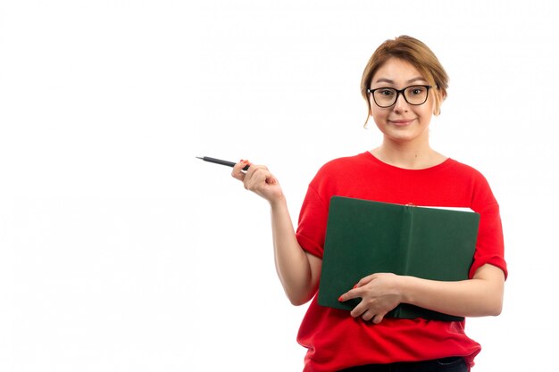 Une vue de face jeune étudiante en t-shirt rouge tenant un cahier souriant sur le blanc