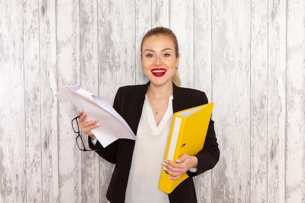 Vue de face jeune femme d'affaires dans des vêtements stricts veste noire document de lecture sur un bureau blanc