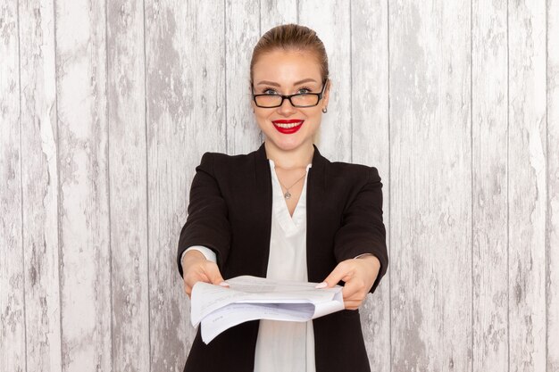 Photo gratuite vue de face jeune femme d'affaires dans des vêtements stricts veste noire donnant un document souriant sur une surface blanche