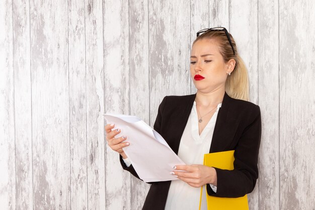 Vue de face jeune femme d'affaires dans des vêtements stricts veste noire lecture document sur surface blanche