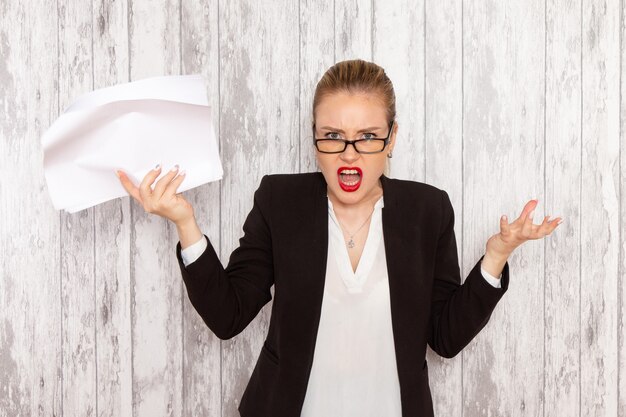 Vue de face jeune femme d'affaires dans des vêtements stricts veste noire lecture document sur surface blanche