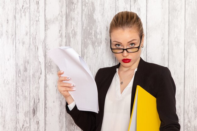 Vue de face jeune femme d'affaires dans des vêtements stricts veste noire lecture document sur surface blanche