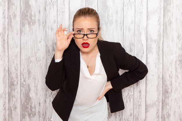 Photo gratuite vue de face jeune femme d'affaires dans des vêtements stricts veste noire avec des lunettes de soleil optiques posant sur mur blanc travail travail bureau entreprise