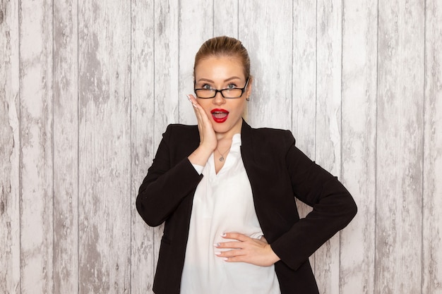 Vue de face jeune femme d'affaires dans des vêtements stricts veste noire avec des lunettes de soleil optiques posant sur mur blanc travail travail bureau femme entreprise