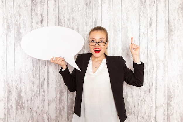 Photo gratuite vue de face jeune femme d'affaires dans des vêtements stricts veste noire tenant énorme panneau blanc sur un bureau blanc